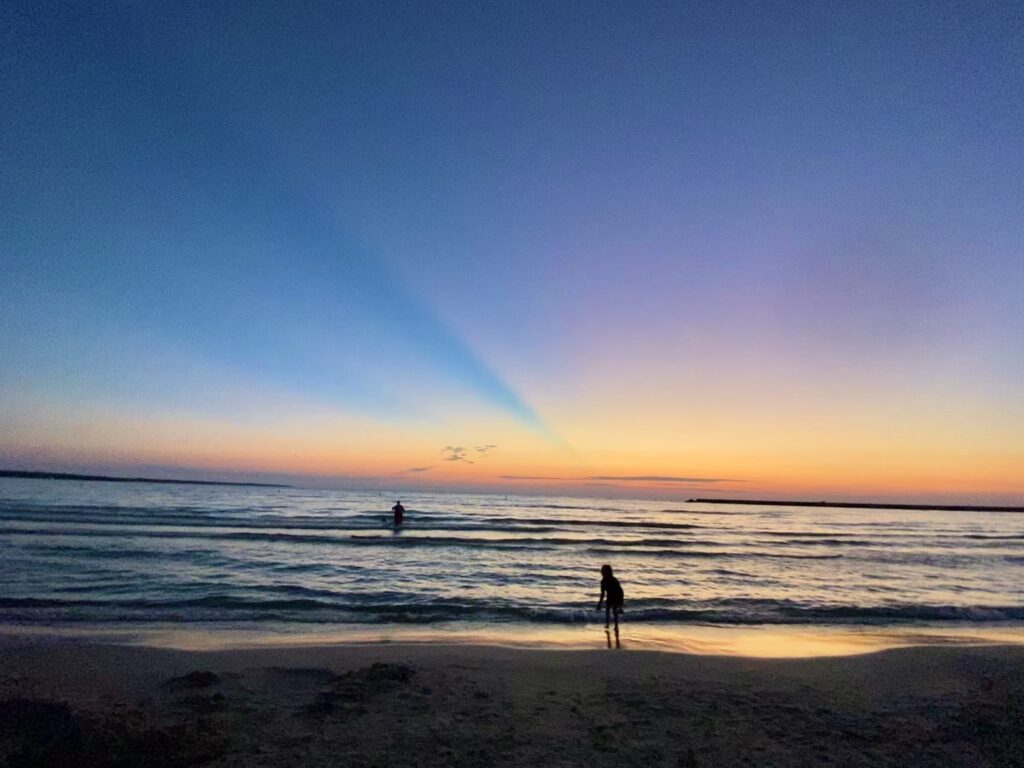 Two people play in the water at a beach at sunset.