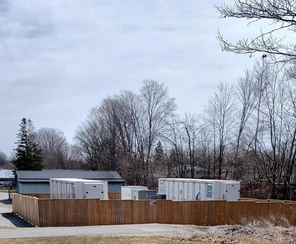 Large grey boxes sit on the ground surrounded by a wooden fence. 