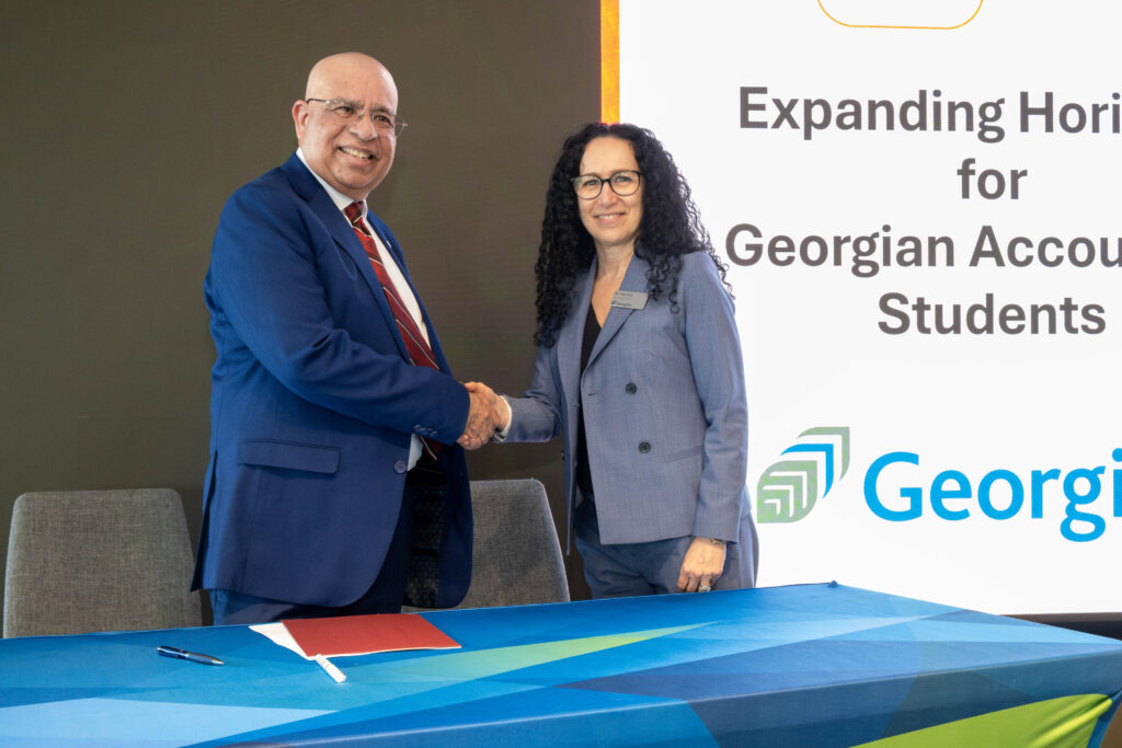 Two people stand behind a table and shake hands.