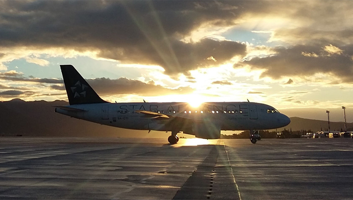 A Star Alliance commercial airplane sitting on an airport runway with a sunset in the background