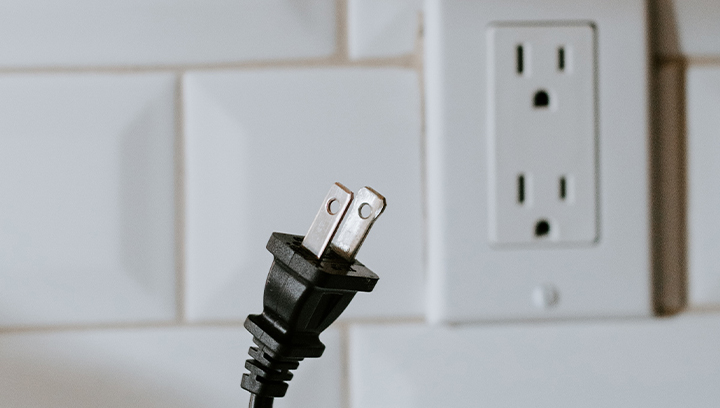 A white dual electrical outlet/socket on a white tile backsplash, with a black plug