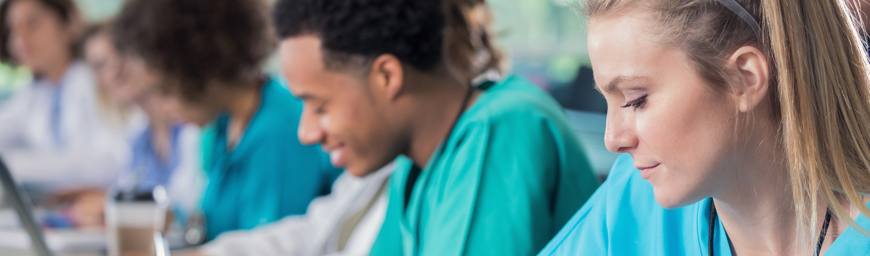 A group of students sitting at desks wearing blue, turquoise and white medical scrubs