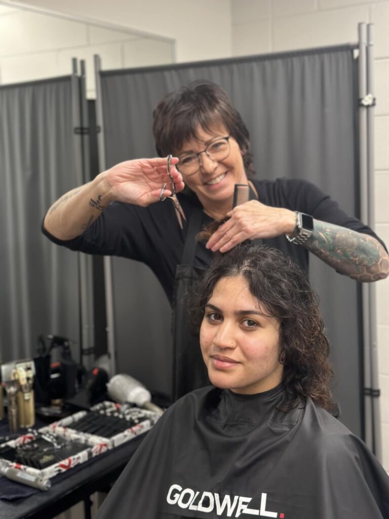 A hair stylist holds a pair of scissors and holds some hair of a person sitting in a chair. 