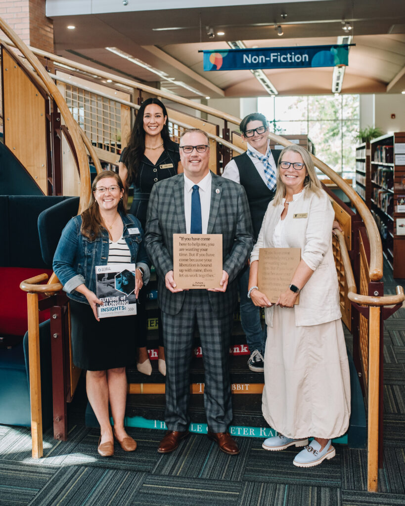 Five people stand together on a winding staircase inside a library. 