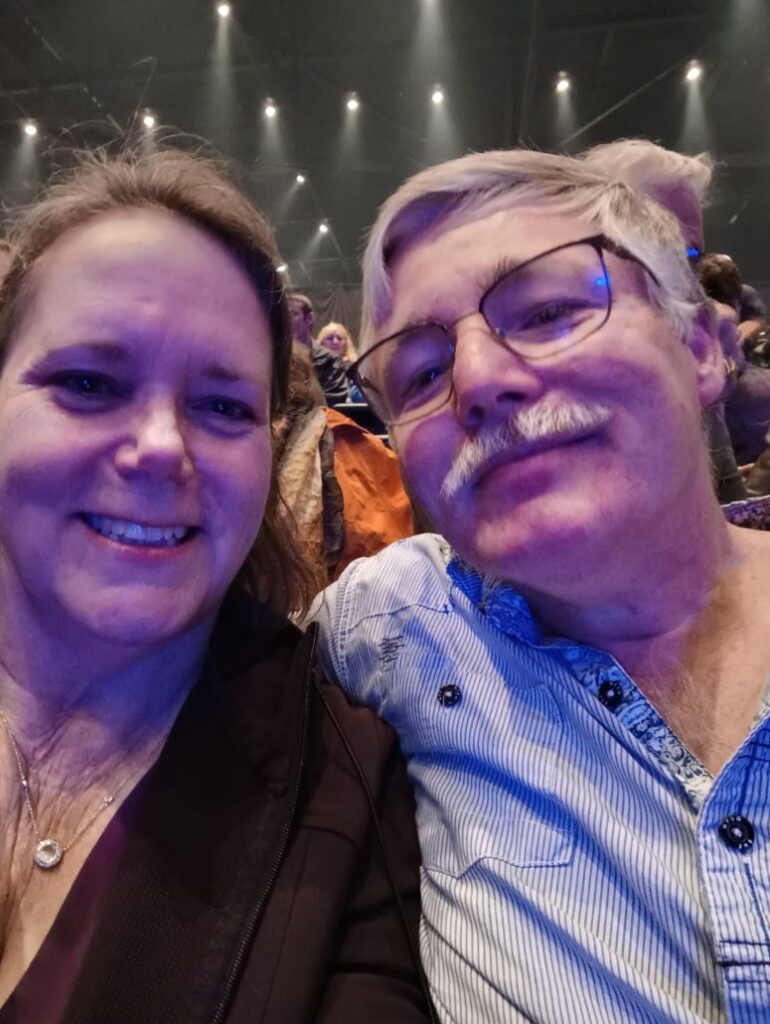 Two people take a selfie while sitting in a concert venue.
