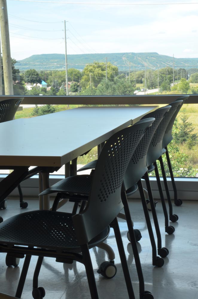 two tables pushed together with four chairs in front of a window with mountainview scenery on a summer day