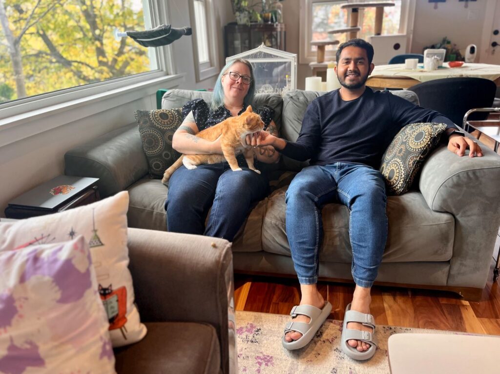Two people and a cat sit on a couch inside a house.