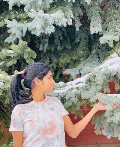 Student board representative, Karthika, outside hand touching a spruce tree