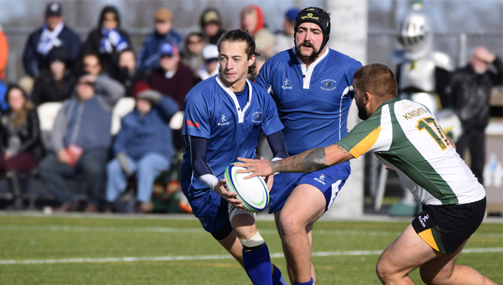 three male students playing varsity rugby on a sports field