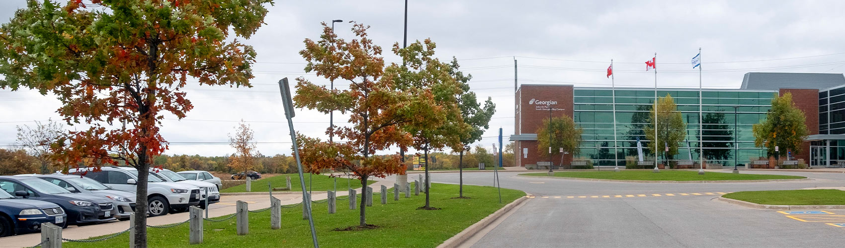 exterior of the Georgian College South Georgian Bay Campus in the fall featuring flags, parked vehicles, green grass and trees