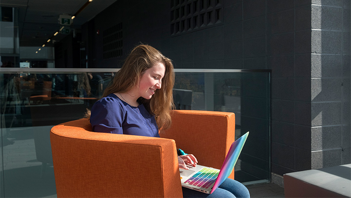 student sitting on an orange lounge chair in N building at the Barrie Campus using a laptop computer