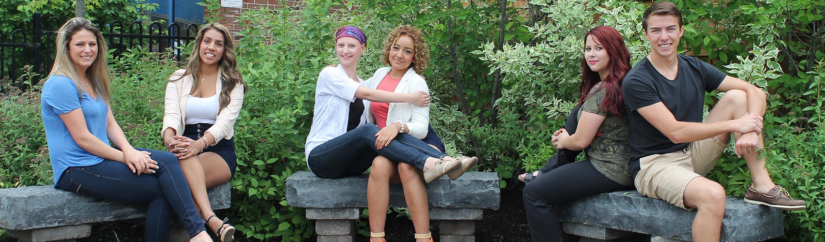 six college students sitting on stone benches in front of plants and bushes