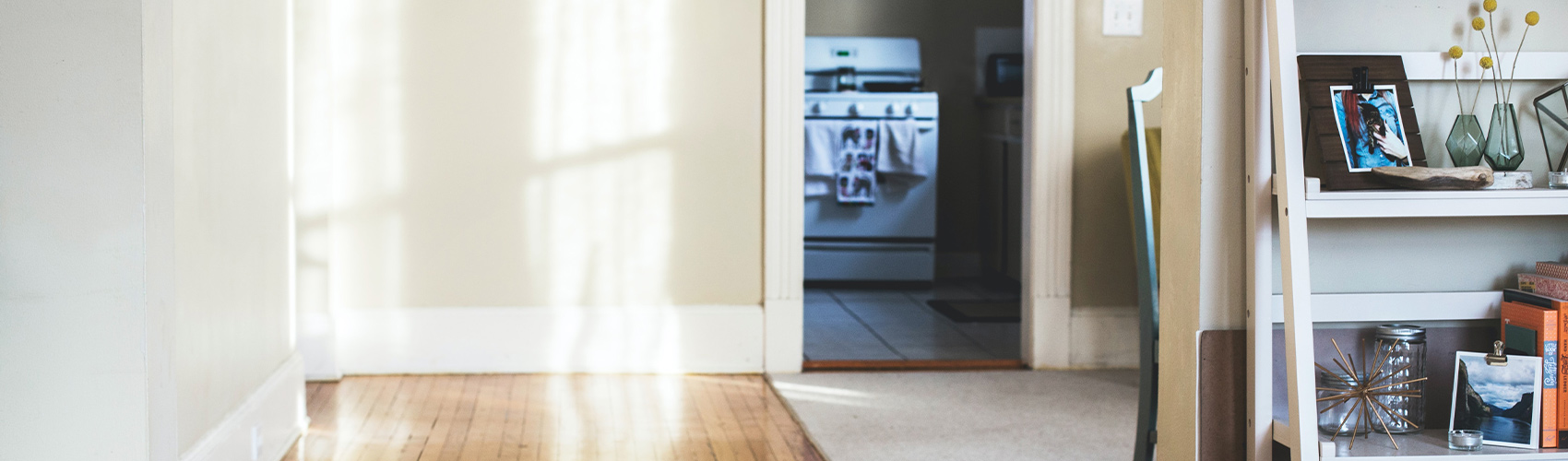 student housing showing beige walls, hardwood floors, a shelf with decorations and a stove with towels hanging