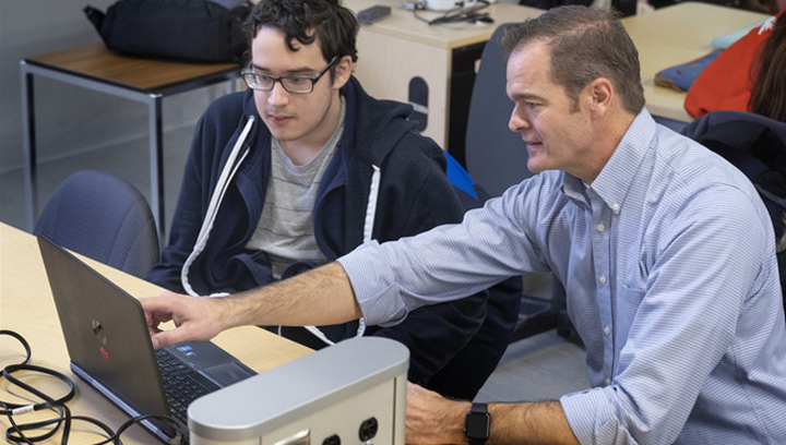 two males looking at a laptop computer with one pointing to the screen