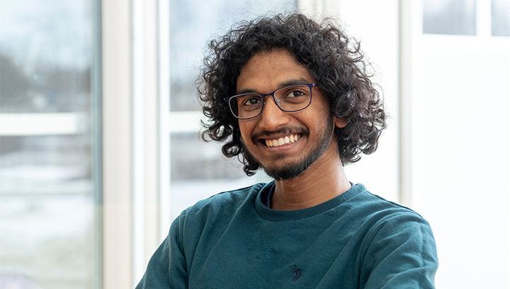 a male international student with dark brown curly hair and glasses smiling