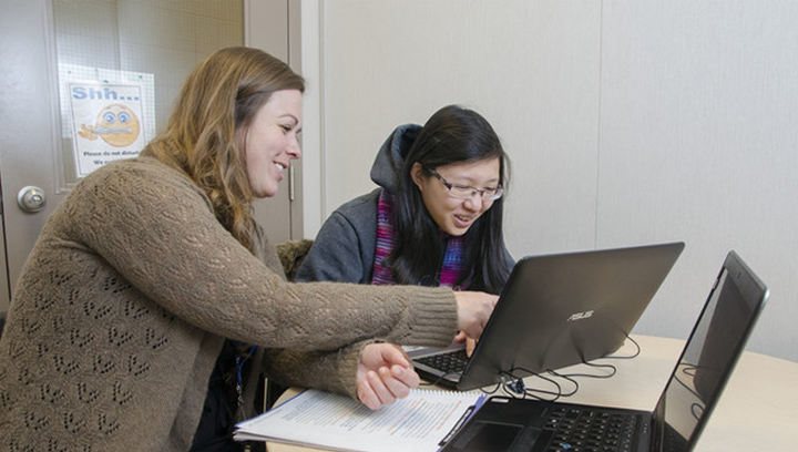 a tutor helping a student with coursework with laptops and a book