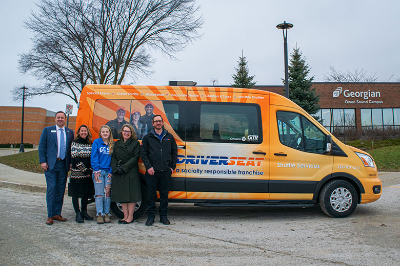Five people standing in front of a colourful van parked in front of the Owen Sound Campus. Dave Shorey, Madison Kittel and Madison Lindsay are in the picture.