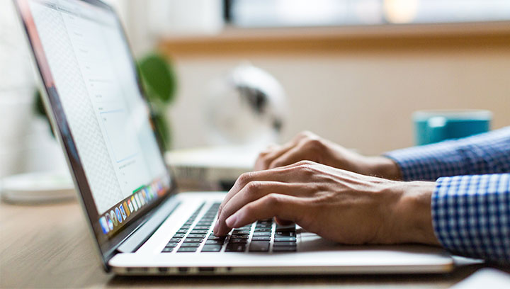 Student at a desk typing on a laptop to complete online courses