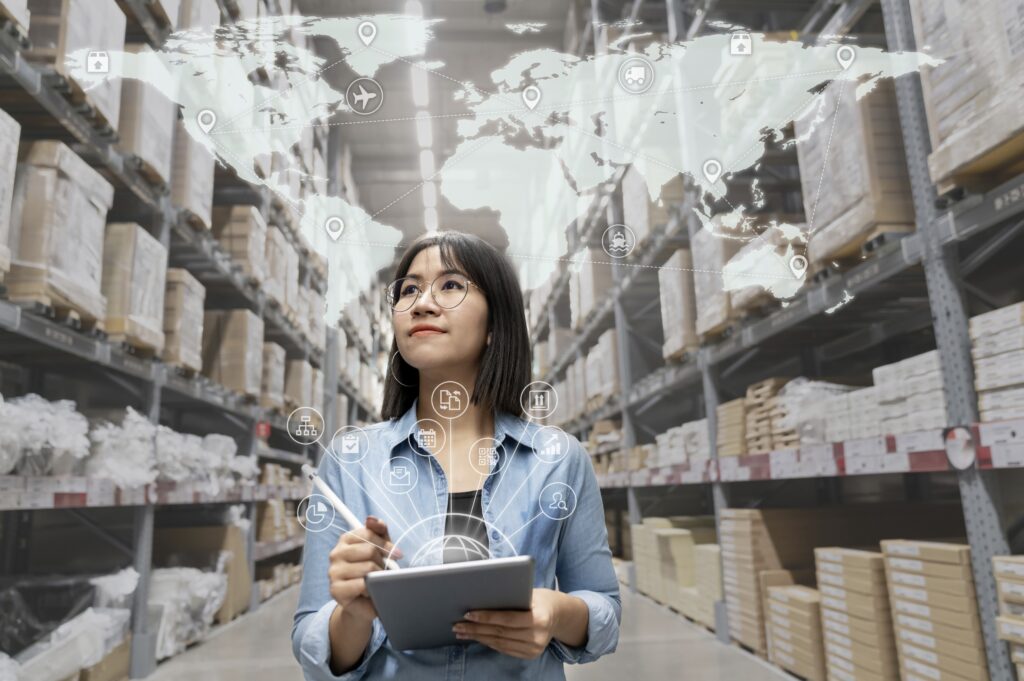 A person holding a clipboard stands in an aisle in a warehouse, with an image of the continents and circles overlaid above their head. 