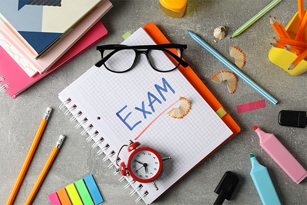 notebook with exam written on it, surrounded by various stationary items