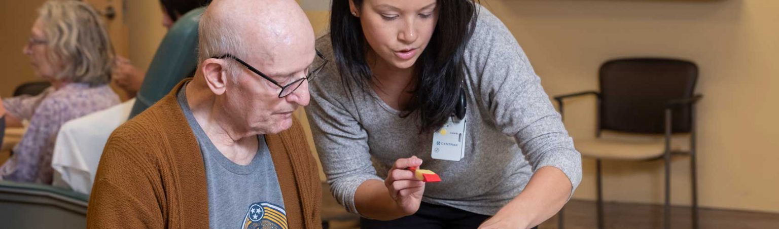 A Therapeutic Recreation student assisting an elderly man with a painting exercise in a care facility