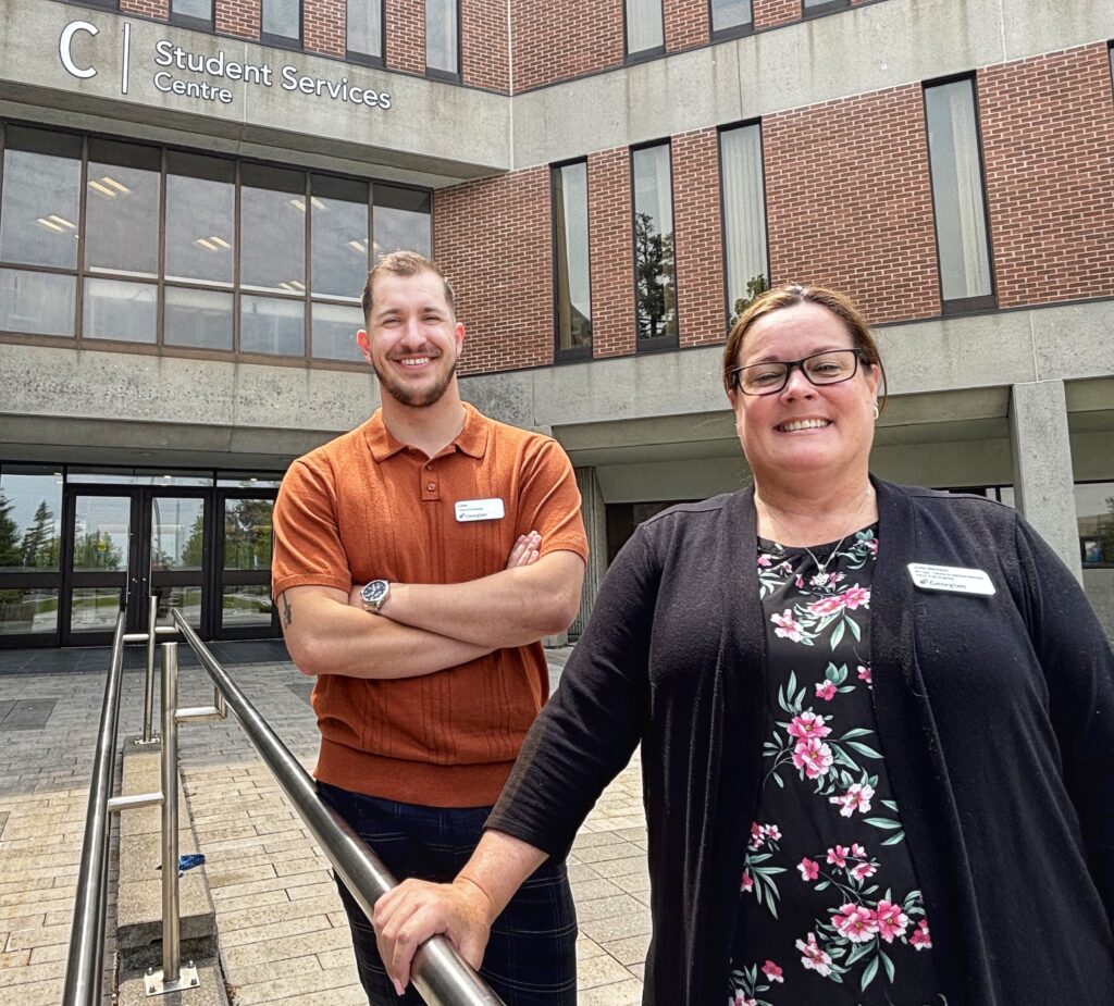 Two people stand outside a building and smile.