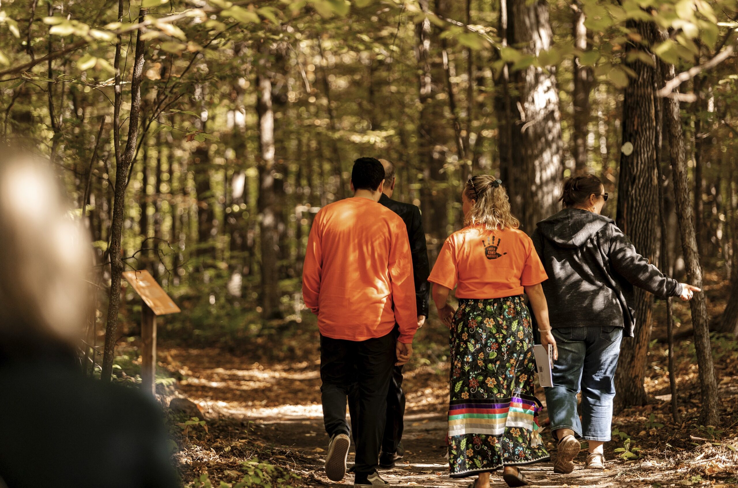 People in orange shirts walk along a wooded trail. 