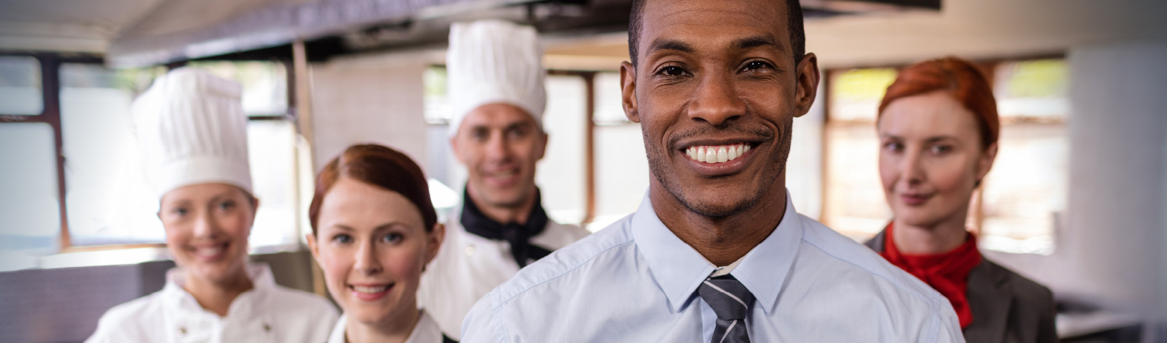 A group of workers in the hospitality and tourism sector in uniform (e.g. chef, manager, server) while standing inside a kitchen