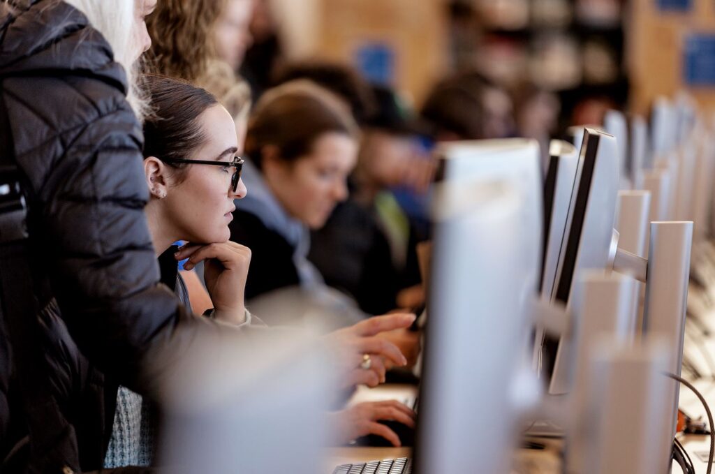 A row of people sit or stand at computers.