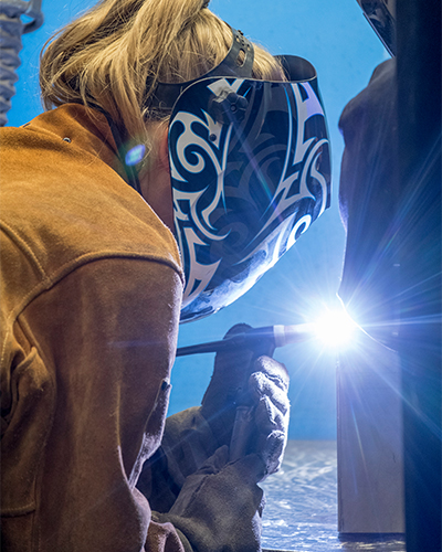 A Welding Techniques student at Georgian College wearing a welding helmet and soldering tool, training to become a welder upon graduation